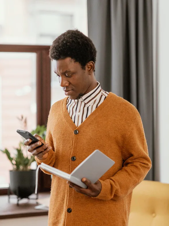 A man holding a book and using his phone